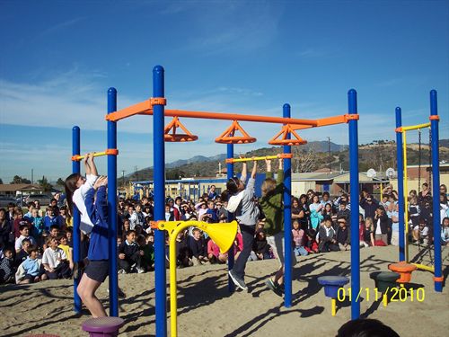 students using the monkey bars and group of students sitting on the playground watching